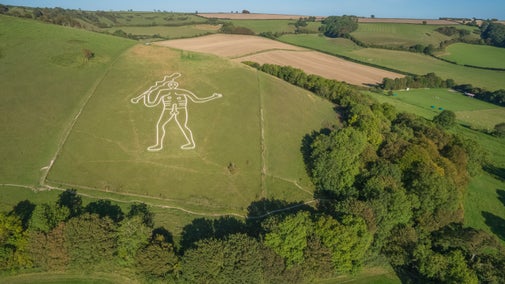 Aerial view of Cerne Abbas chalk giant after being re-chalked surrounded by fields and woodland in early autumn in Dorset.
